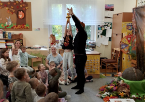 Pan podnosi do góry chłopca, który trzyma się przyssawek, aby pokazać dzieciom jak silne są mrówki.