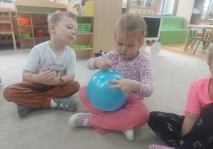 Dziewczynka maluje na balonie emotkę ze smutkiem.