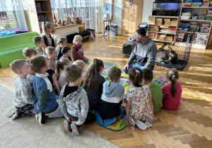Dzieci siedzą w kole i słuchają pana.