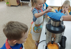 Dzieci wkładają do pojemnika obrane jabłka i marchewkę.