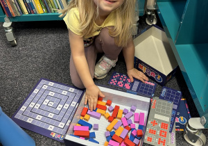 Dziewczynka rozkłada elementy gry na dywanie.
