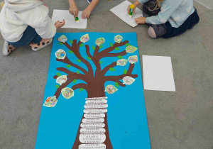 Dzieci przyklejają kolorowanki praw do drzewka.