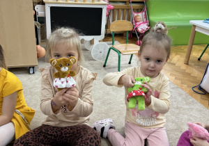 Dziewczynki pokazują misia w spódniczce.