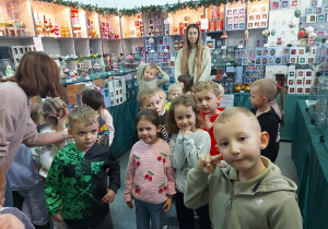 Dzieci stoją z panią w sklepiku w fabryce bombek.
