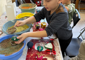 Chłopiec obsypuje bombkę brokatem.