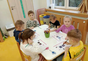 Dzieci rozwiązują kartę pracy przy stoliczku.