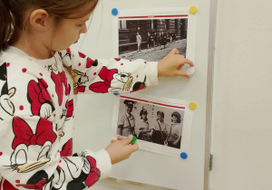 Dziewczynka przyczepia zdjęcie na tablicy.