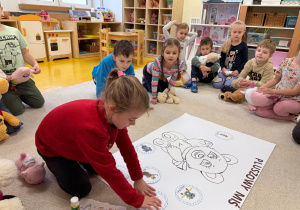 Dziewczynka przykleja misia na plakat.