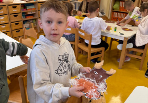 Chłopiec prezentuje swoją prace plastyczną.