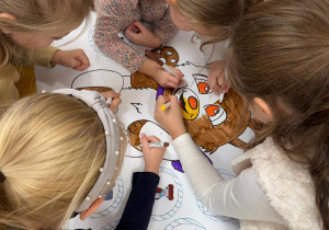 Dziewczynki kolorują misia na plakacie.