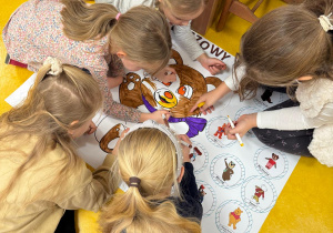 Dziewczynki kolorują misia na plakacie.