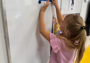 Dziewczynka zawiesza zdjęcie na tablicy.