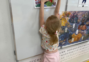 Dziewczynka zawiesza zdjęcie na tablicy.
