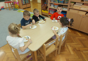 Dzieci siedzą przy stoliku i jedzą tort.