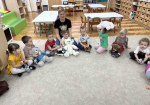 Dzieci z misiami siedzą na dywanie.