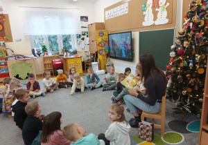 Dzieci siedzą w kole i z zainteresowaniem słuchają bajki.