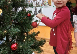 10. Dziewczynka zawiesza ozdobę na choinkę.