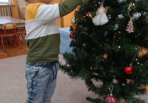 13. Chłopiec zawiesza ozdobę na choinkę.