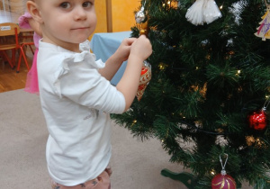 15. Dziewczynka zawiesza ozdobę na choinkę.