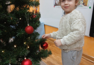 16. Chłopiec zawiesza czerwoną bombkę na choinkę.