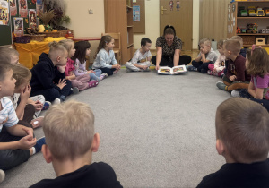 Dzieci siedzą w kole i słuchają bajki czytanej przez mamę jednego z chłopców.