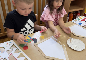 Chłopiec i dziewczynka tworzą ptaka z wyciętych elementów.