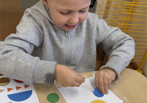 Chłopiec przykleja papierowe części tworząc ptaka.