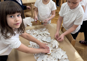 Dzieci układają z liści flagę Polski.