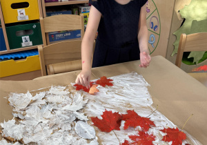 Dziewczynka przykleja czerwone liście.