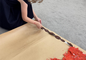 Dziewczynka układa uchwyt flagi z brązowych liści.