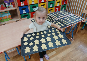 Dziewczynka trzyma blachę z ciasteczkami.