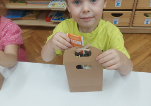 Chłopiec z grupy 4 latków wkłada herbatkę do pudełka.