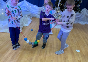 Chłopcy nawlekają bombki na sznurek tworząc łańcuch.