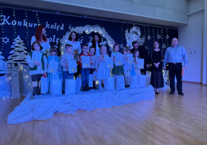 Dzieci stoją na scenie z dyplomami i statuetkami.