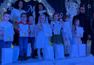 Uśmiechnięci uczestnicy na scenie z nagrodami.