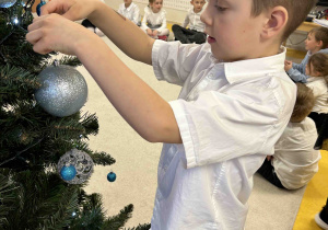 Chłopiec zawiesza bombkę na choinkę.