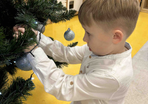 Chłopiec zawiesza bombkę na choinkę.