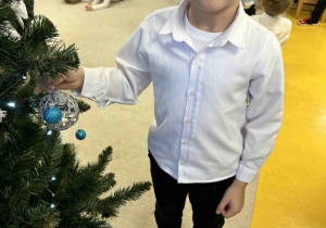 Uśmiechnięty chłopiec stoi koło choinki.