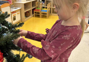 Dziewczynka zawiesza bombkę na choinkę.