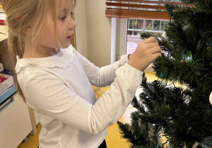 Dziewczynka zawiesza bombkę na choinkę.