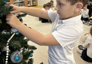 Chłopiec przyozdabia choinkę w sali.