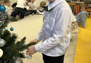 Chłopiec przyozdabia choinkę w sali.