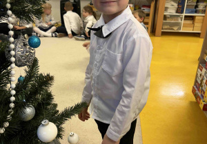 Zadowolony chłopczyk stoi koło ubranej choinki.