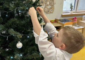 Chłopiec przyozdabia choinkę w sali.