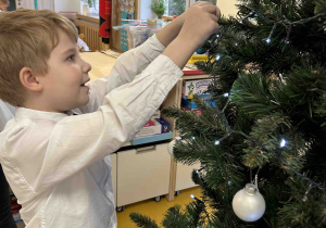 Chłopiec przyozdabia choinkę w sali.