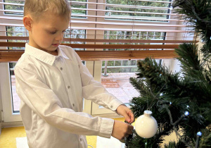 Chłopiec zawiesza bombkę na drzewku.