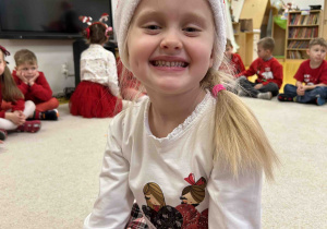Uśmiechnięta dziewczynka w czapce Mikołaja.