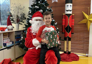 Uśmiechnięty chłopiec siedzi na kolanach u Mikołaja.