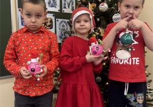Chłopcy i dziewczynka prezentują gotowe bombki przy choince.