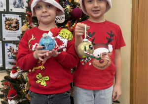 Chłopcy stoją przy choince i pokazują wykonane przez siebie bombki.